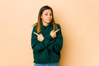 Bej arka plan noktalarında izole edilmiş genç bir kadın iki seçenek arasında seçim yapmaya çalışıyor..