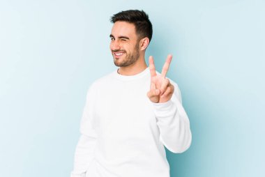 Mavi arka planda izole edilmiş genç beyaz adam iki numarayı parmaklarıyla gösteriyor..
