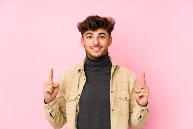 Arka planda poz veren genç Arap bir adam, iki ön parmağı da boş bir alan gösterirken,.