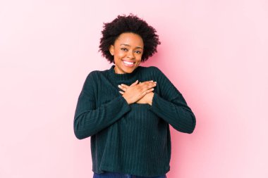 Orta yaşlı Afro-Amerikalı kadın pembe arka planda yalnız, dost bir ifadeye sahip, avuçlarını göğsüne bastırıyor. Aşk konsepti.
