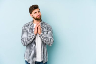 Kafkasyalı genç bir adam mavi arka planda izole edildi. Aklında bir plan kuruyor, bir fikir kuruyor..