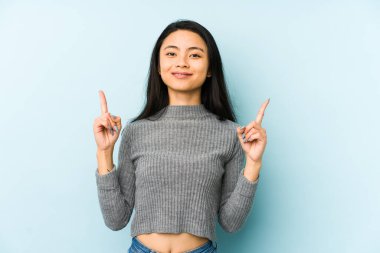 Mavi bir arka planda izole edilmiş genç Çinli kadın iki parmağı da boş bir alan gösteriyor..