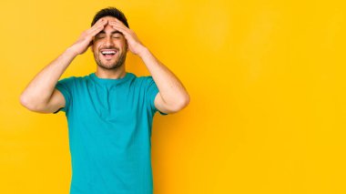 Sarı fırında izole edilmiş genç beyaz adam ellerini başının üstünde tutarak neşeyle gülüyor. Mutluluk kavramı.