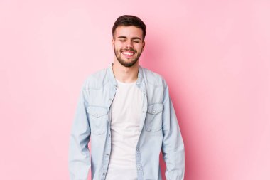 Beyaz arka planda poz veren beyaz tenli genç iş adamı yalnız gülüyor ve gözlerini kapatıyor, rahatlamış ve mutlu hissediyor.