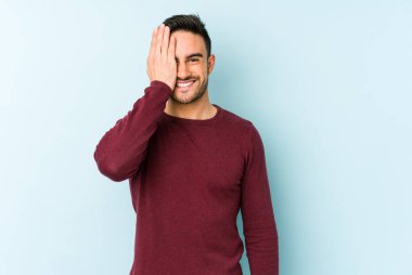 Mavi arka planda izole edilmiş genç beyaz adam yüzünün yarısını palmiye ile kaplayarak eğleniyor..