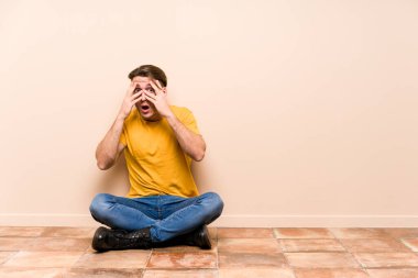 Yerde oturan genç, beyaz bir adam yalnız. Korkmuş ve gergin parmaklarıyla göz kırp..