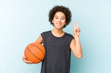 Çocuk basketbol oynuyor. Mavi arka planda izole edilmiş. İki numarayı parmaklarıyla gösteriyor..