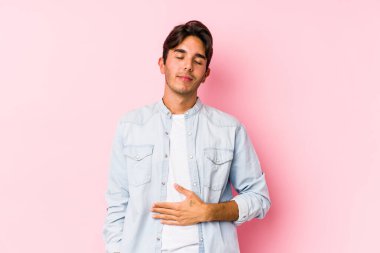 Pembe arka planda poz veren beyaz bir genç göbeğe dokunuyor, nazikçe gülümsüyor, yemek yiyor ve tatmin oluyor..