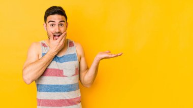 Sarı fırında izole edilmiş genç beyaz bir adam bir avuç içinde fotokopi alanı tutuyor, el üstünde tutuyor. Şaşırmış ve mutlu..