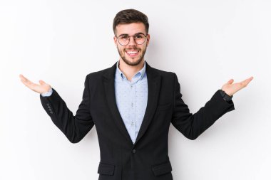 Beyaz arka planda poz veren beyaz tenli genç beyaz iş adamı genç beyaz iş adamı kollarıyla ölçek yapıyor, mutlu ve kendinden emin hissediyor..