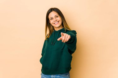 Bej arka planda izole edilmiş genç bir kadın parmaklarıyla ön tarafı işaret ediyor..