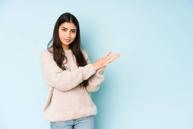 Mavi arka planda izole edilmiş genç Hintli kadın enerjik ve rahat hissediyor, ellerini ovuşturuyor..