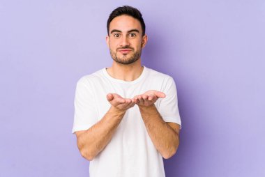 Mor arka planda izole edilmiş genç beyaz adam dudakları katlıyor ve hava öpücüğü göndermek için avuç içleri tutuyor..