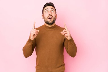 Pembe arka planı olan beyaz bir genç, ağzı açık, üst tarafı göstererek izole edilmiş..