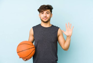 Beş numarayı parmaklarıyla gülümseyerek basket oynayan genç bir Arap..