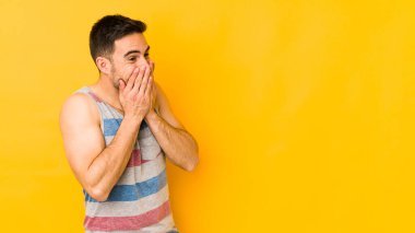 Sarı fırında izole edilmiş genç beyaz bir adam bir şeye gülüyor, elleriyle ağzını kapatıyor..