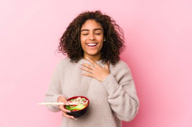 Genç Afrikalı Amerikalı kadın erişte yerken yüksek sesle gülüyor ve elini göğsüne koyuyor..