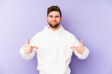 Mor arka planda izole olmuş genç beyaz bir adam gömlek fotokopisini elle gösteriyor, gururlu ve kendinden emin.