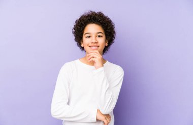 Afrikalı Amerikalı küçük çocuk yalnız başına mutlu ve kendinden emin gülümsüyor, elleriyle çenesine dokunuyor..