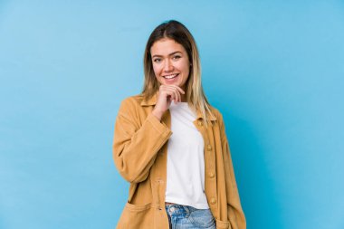 Genç beyaz kadın mutlu ve kendinden emin gülümsüyor, elleriyle çenesine dokunuyor..