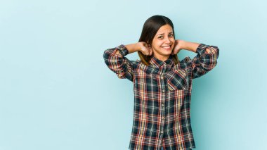 Mavi arka planda izole edilmiş genç bir kadın kafasının arkasına dokunuyor, düşünüyor ve bir seçim yapıyor..