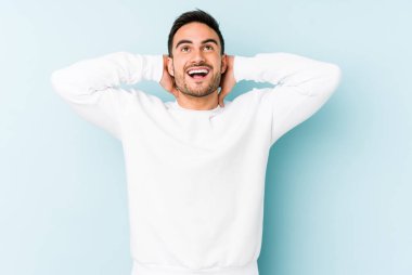 Kafkasyalı genç adam mavi arka planda izole edilmiş. Kendine güveniyor, elleri başının arkasında..