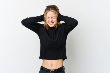 Beyaz arka plandaki genç beyaz kadın kulaklarını elleriyle kapatıyor ve çok fazla ses duymamaya çalışıyor..