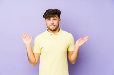 Mor arka planda izole edilmiş genç Arap bir adam. Kopya alanını tutmak için kafası karışık ve omuz silkiyor..