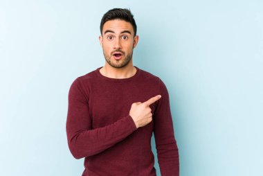 Mavi arka planda izole edilmiş genç beyaz adam yan tarafı işaret ediyor.