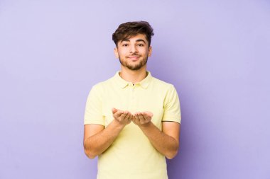 Mor arka planda izole edilmiş genç bir Arap adam elinde avuç içi bir şeyle kameraya sunuyor..