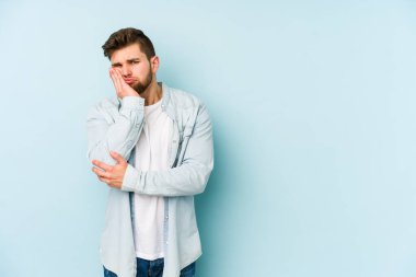 Mavi arka planda izole edilmiş, sıkılmış, yorgun ve dinlenmeye ihtiyacı olan genç beyaz bir adam..