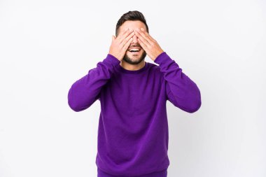 Beyaz bir arka planı olan beyaz tenli genç bir adam, gözleri kapalı, gülümseyerek bir sürpriz bekliyor..