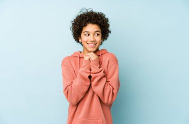 Afrika kökenli Amerikalı küçük çocuk ellerini çenesinin altında tutuyor ve mutlu bir şekilde yan tarafa bakıyor..