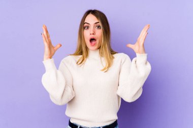 Mor arka planda izole genç beyaz kadın zaferi ya da başarıyı kutluyor, şaşırıyor ve şok oluyor..