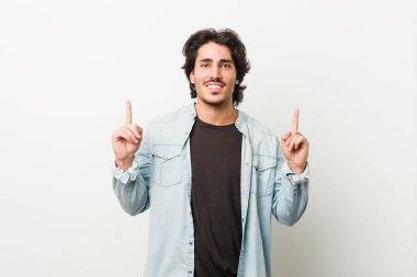 Beyaz bir arka planı olan genç yakışıklı bir adam iki elini de boş bir alan göstererek gösteriyor..