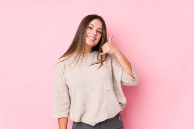 Genç beyaz kadın izole edilmiş poz veriyor. Cep telefonu hareketini parmaklarıyla gösteriyor..