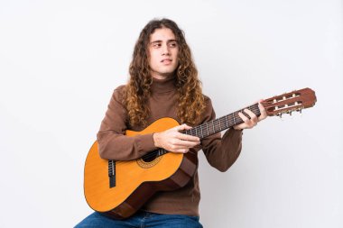 Yalnız başına gitar çalan beyaz bir genç. Gülümsüyor, neşeli ve keyifli görünüyor..