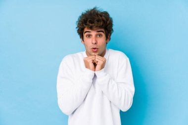Kafkasyalı genç bir adam mavi bir arkaplanda yalnız başına şans diliyor, şaşırıyor ve ağzını açıyor..