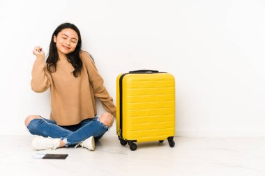 Genç Çinli gezgin kadın bavuluyla yerde oturmuş dans ediyor ve eğleniyor..