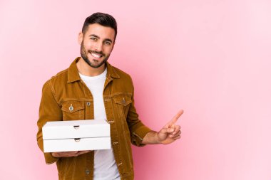 Elinde pizzalarla gezen yakışıklı genç adam gülümsüyor ve boş alanda bir şeyler gösteriyor..