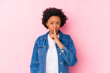 Genç Afrikalı Amerikalı bir kadın pembe bir arka plana karşı izole edilmiş bir şekilde bir sır saklıyor ya da sessizlik istiyor..