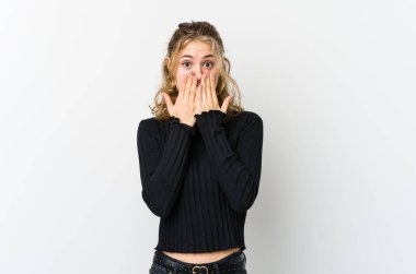 Beyaz arka plandaki genç beyaz kadın şok olmuş, ağzı ellerle kaplanmış, yeni bir şey keşfetmek için sabırsızlanıyor..