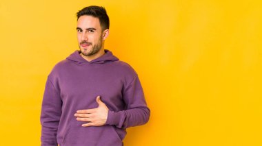 Sarı fırında izole edilmiş genç beyaz adam karnına dokunuyor, nazikçe gülümsüyor, yemek yiyor ve tatmin oluyor..