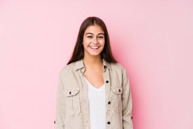 Pembe arka planda poz veren genç beyaz kadın mutlu, güler yüzlü ve neşeli..