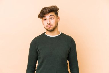 Bej arka planda izole edilmiş genç bir Arap adamın yanakları şişer, yorgun bir ifadesi vardır. Yüz ifadesi kavramı.