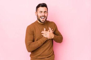 Pembe arka planda genç beyaz bir adam yalnız gülüyor, elini yüreğine koyuyor, mutluluk kavramını koruyor..