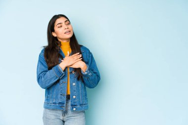 Mavi arka planda izole edilmiş genç Hintli kadın avuçlarını göğsüne bastıran dostça bir ifadeye sahiptir. Aşk konsepti.