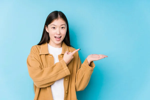 Joven Mujer China Posando Fondo Azul Aislado Excitado Sosteniendo Espacio —  Fotos de Stock