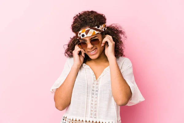 Young african american hipster woman isolated on pink background covering ears with hands.