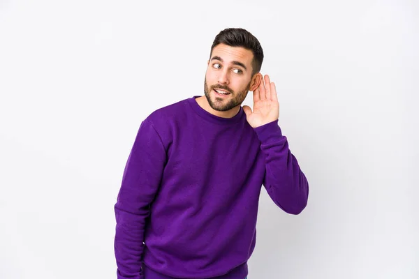 Young caucasian man against a white background isolated trying to listening a gossip.